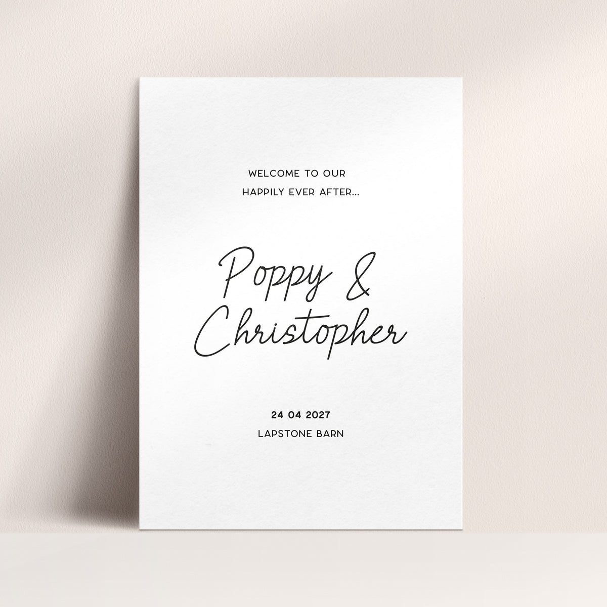 A minimalist white wedding welcome sign with black text reading 'Welcome to our happily ever after.', names and wedding date and venue.