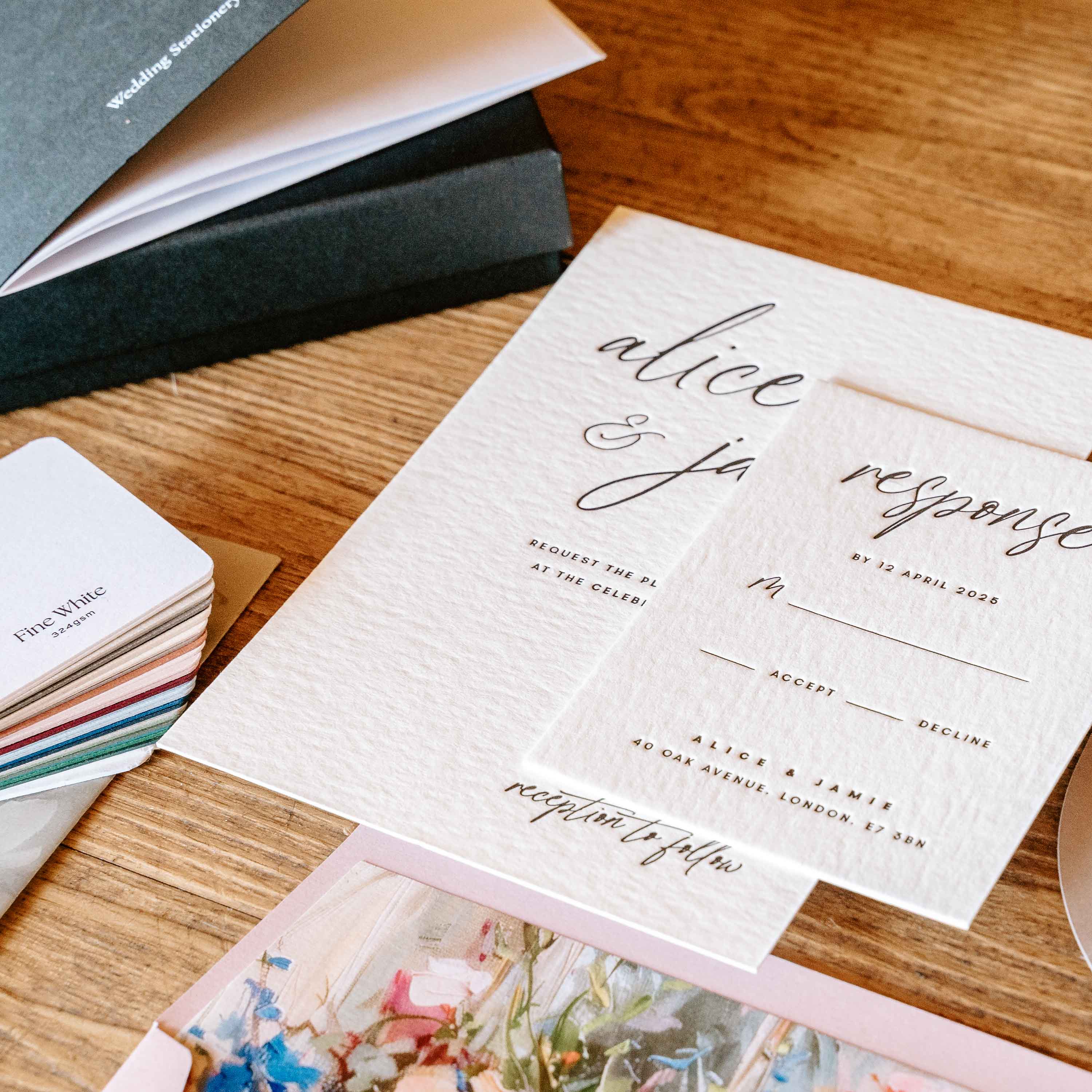 Wedding invitation card with 'alice & jamie' on a wooden surface