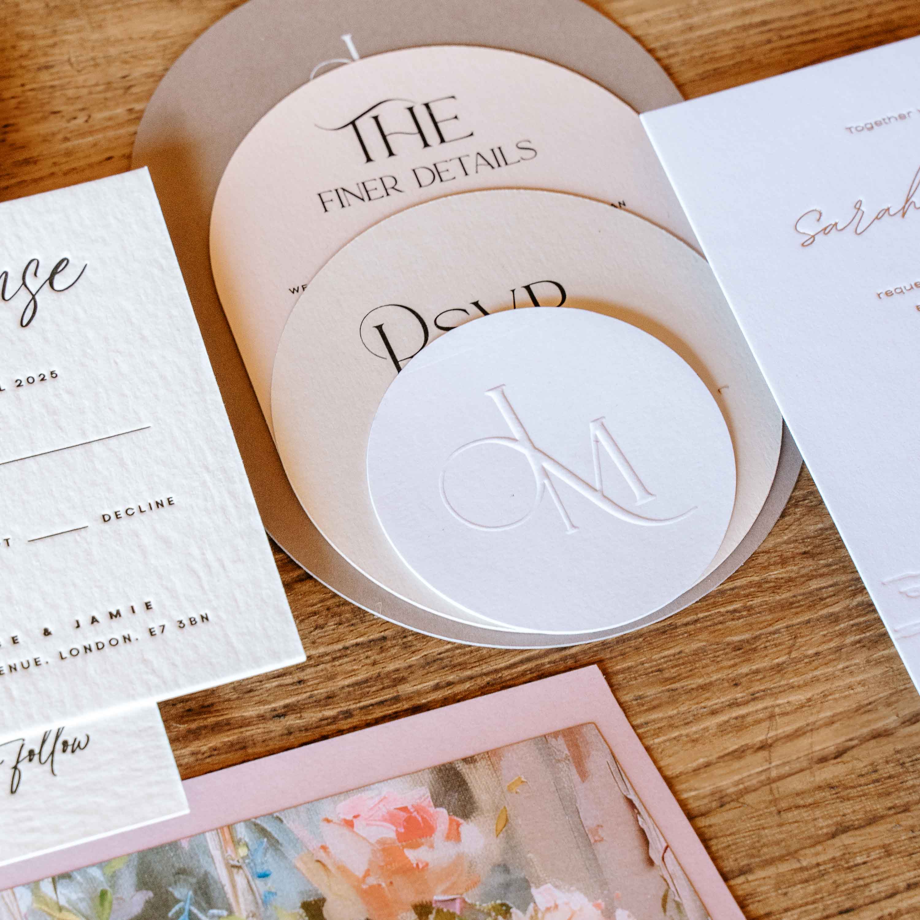 Arched wedding invitation suite with embossed logo on a wooden surface with stationery items.