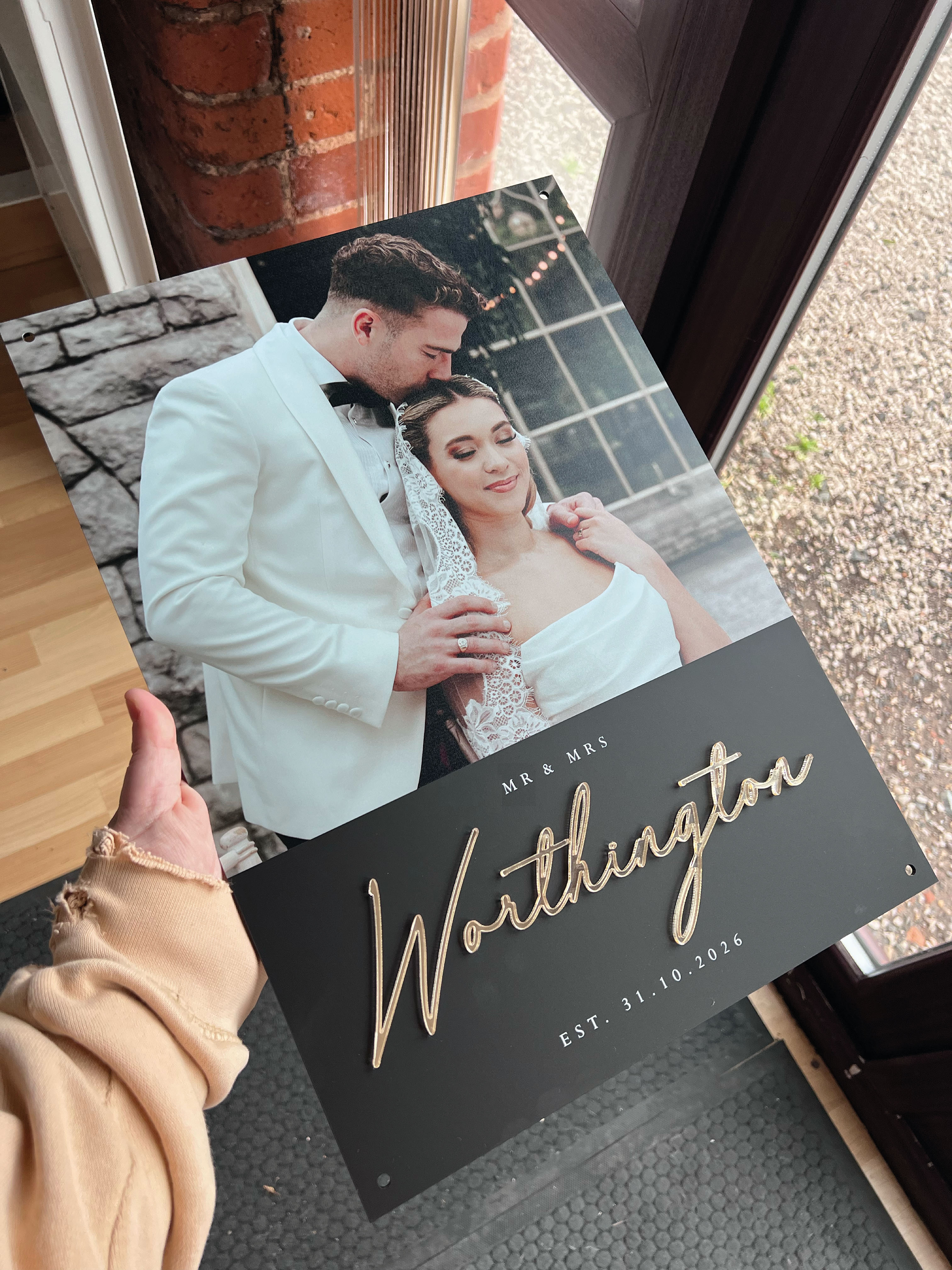 Personalized sign with a couple's name and wedding date, held by a person indoors.