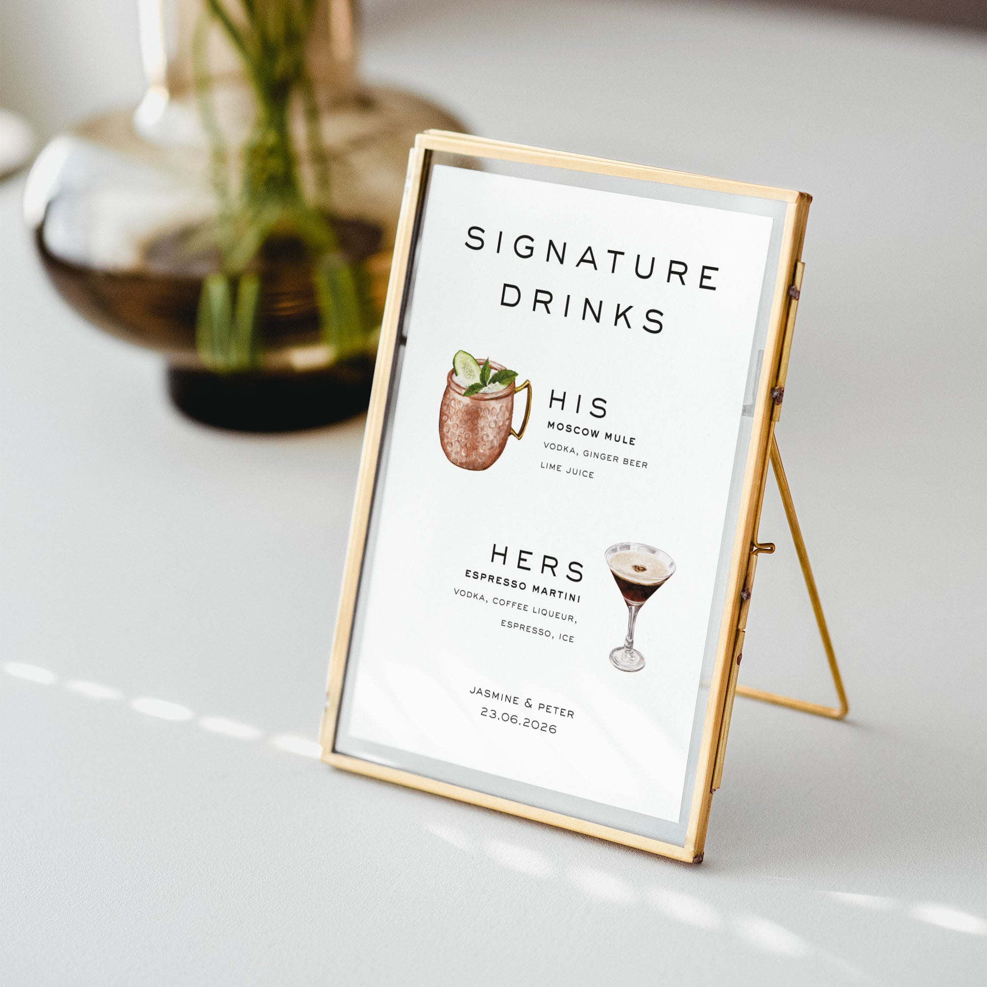 Signature drinks menu for a wedding reception on a stand with a gold frame on a white surface.