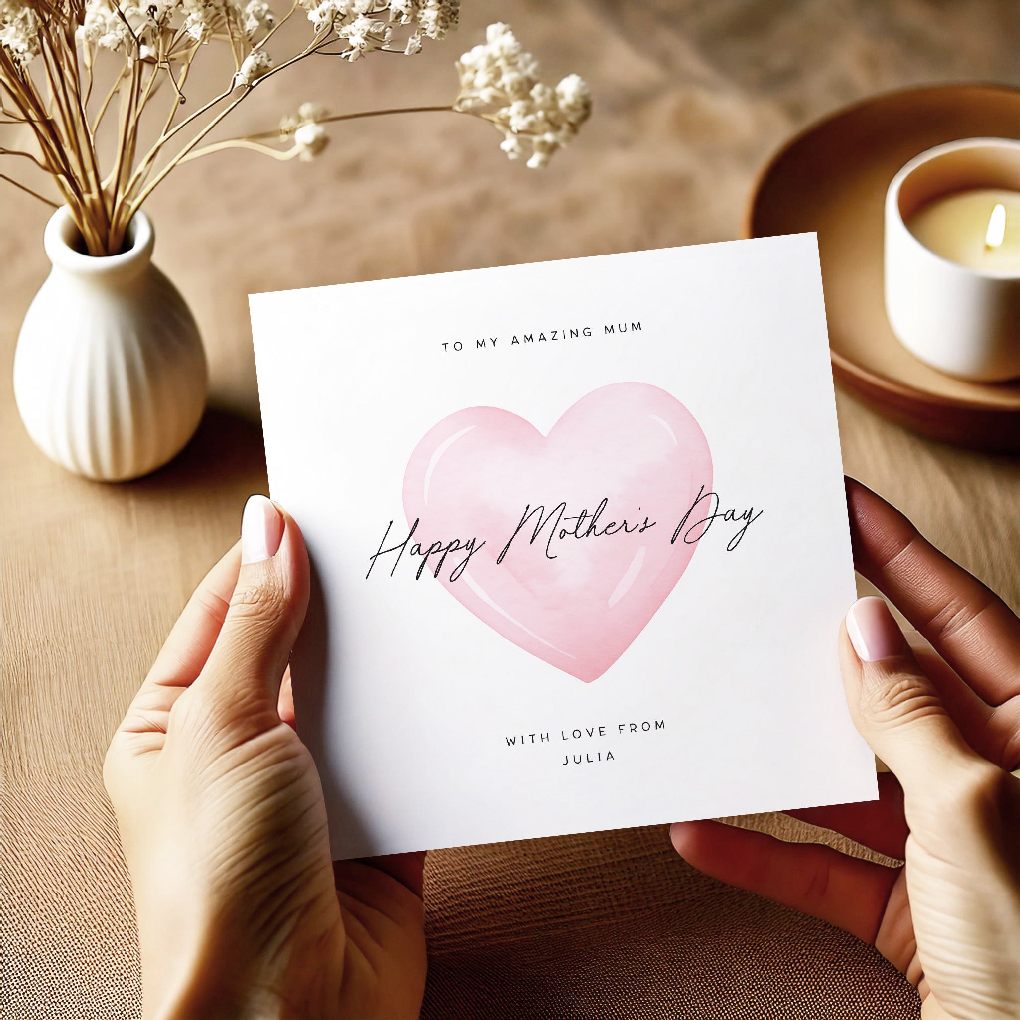 Person holding a Mother's Day card with a pink heart design on a wooden surface.