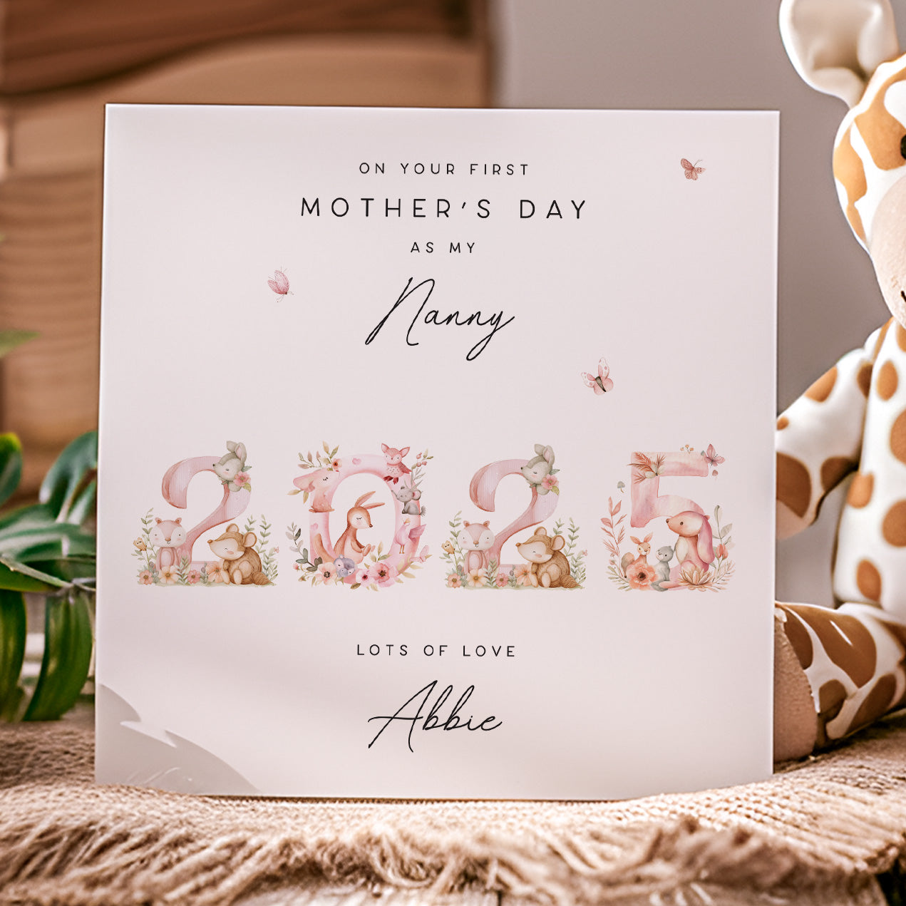 Greeting card for Mother's Day with '2025' and floral elements, placed on a textured surface with a giraffe toy.