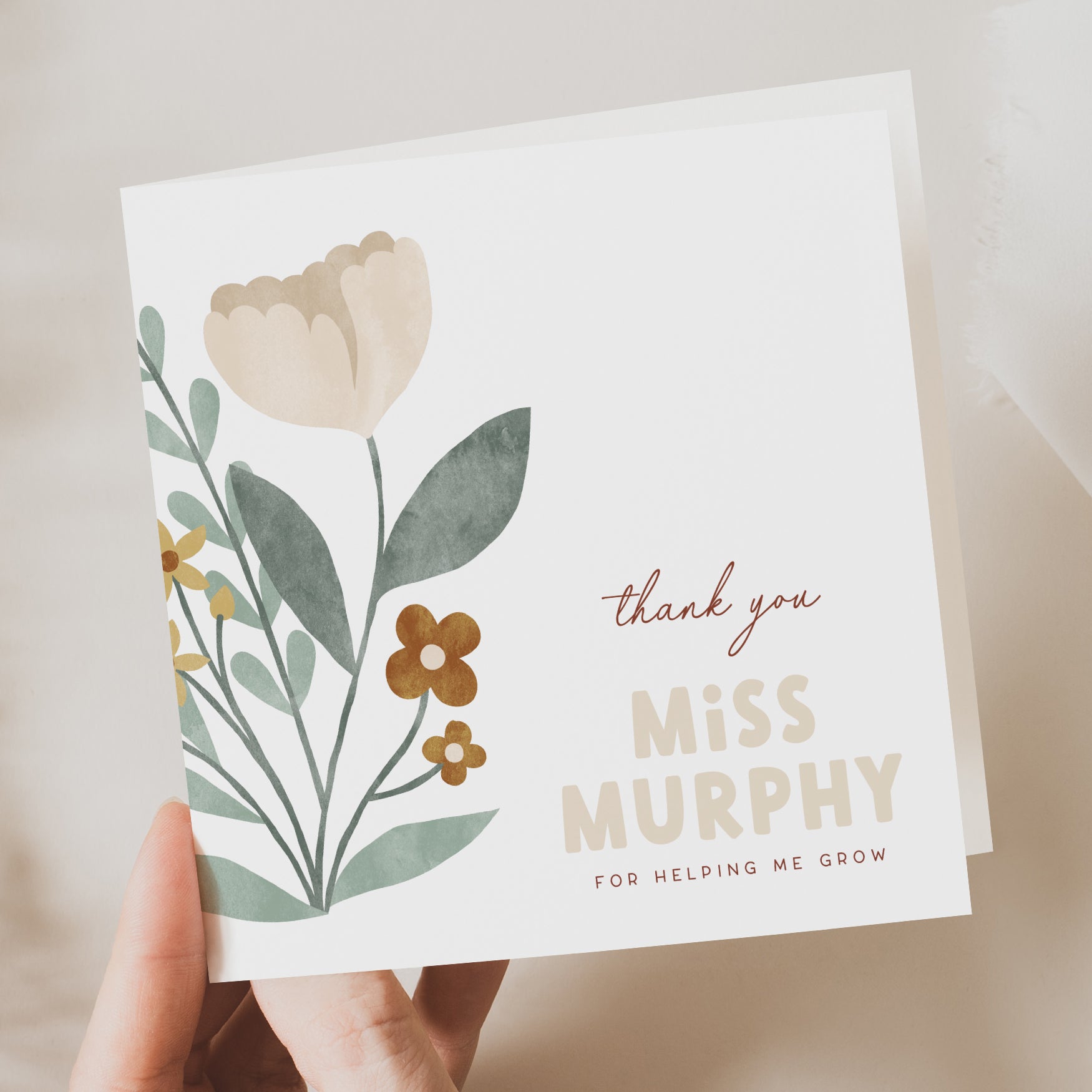 Greeting card with floral design and text held by a hand on a neutral background