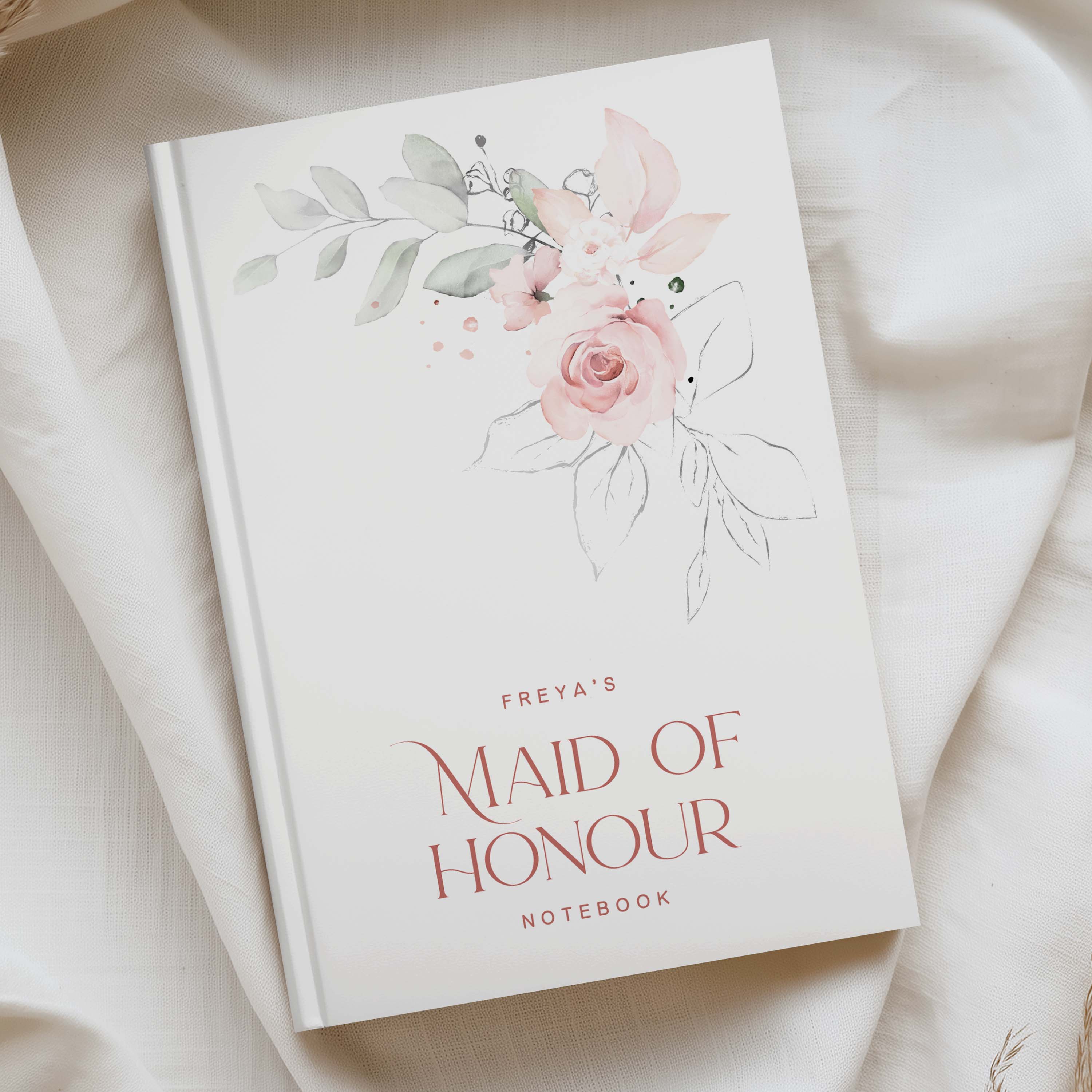 White a5 notebook with pink and green watercolour florals and the phrase "FREYAS MAID OF HONOUR NOTEBOOK" IN RICH PINK TEXT