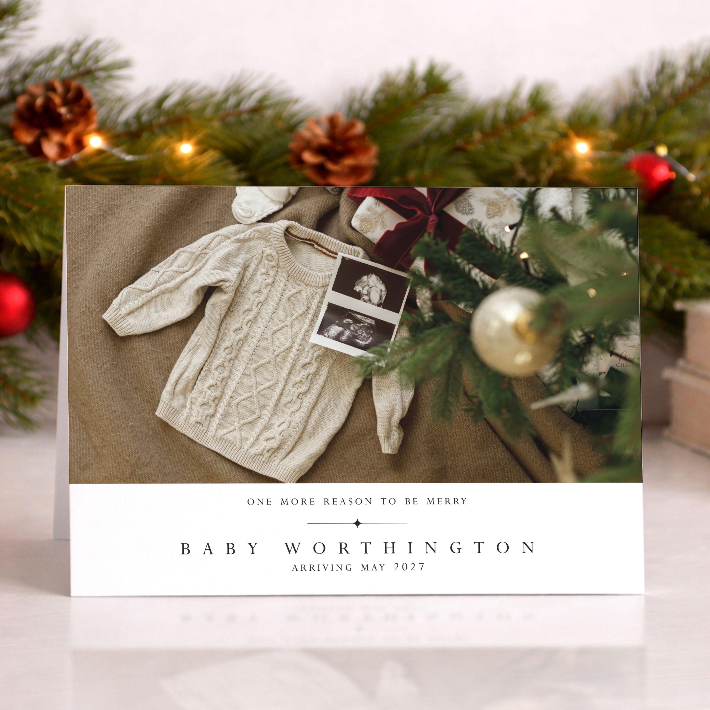 Christmas card with baby announcement featuring a sweater and photo, surrounded by festive decorations.