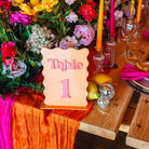 Decorative table setup with flowers, candles, and a table number sign on a wooden table.