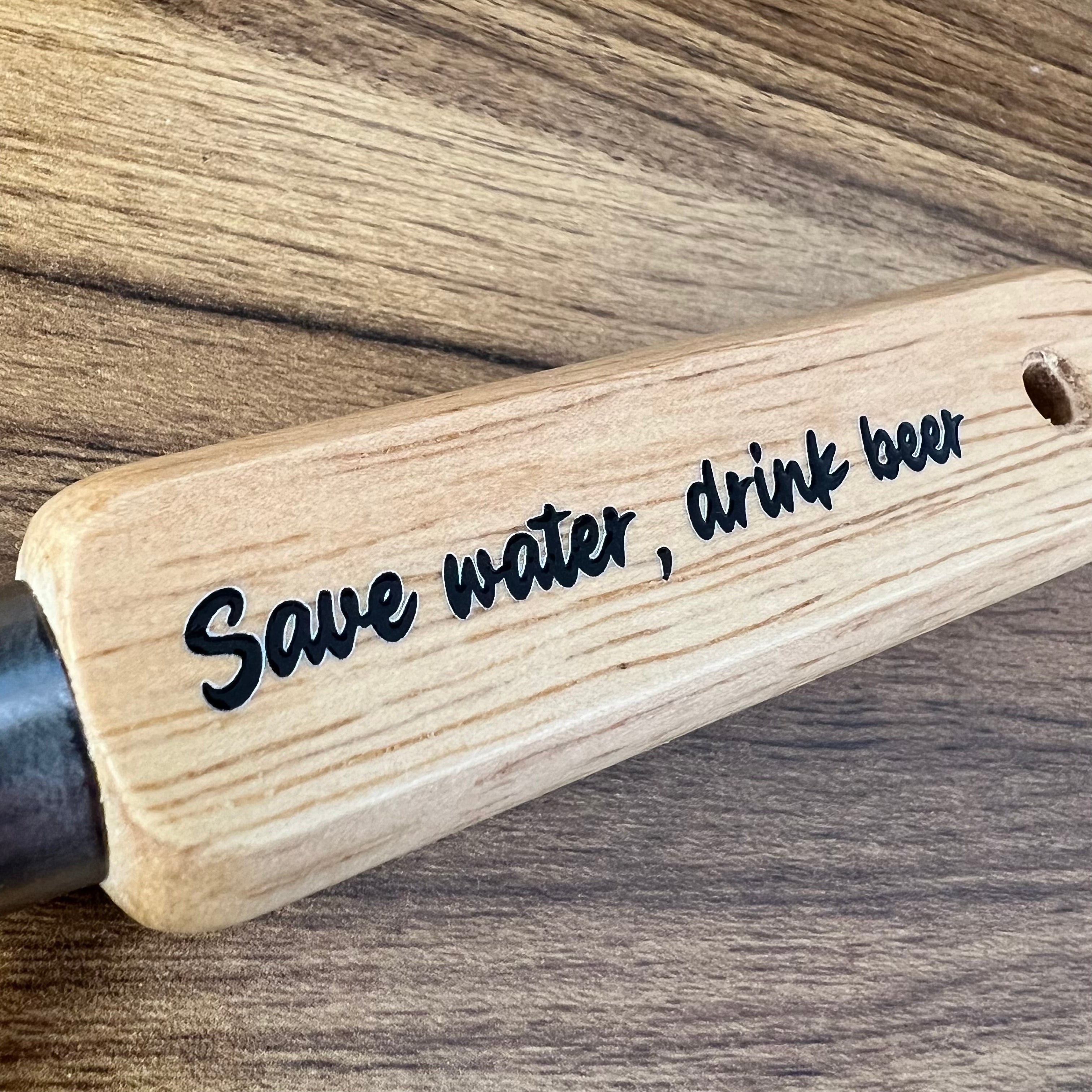 Wooden handle with 'Save water, drink beer' engraving on a wooden background