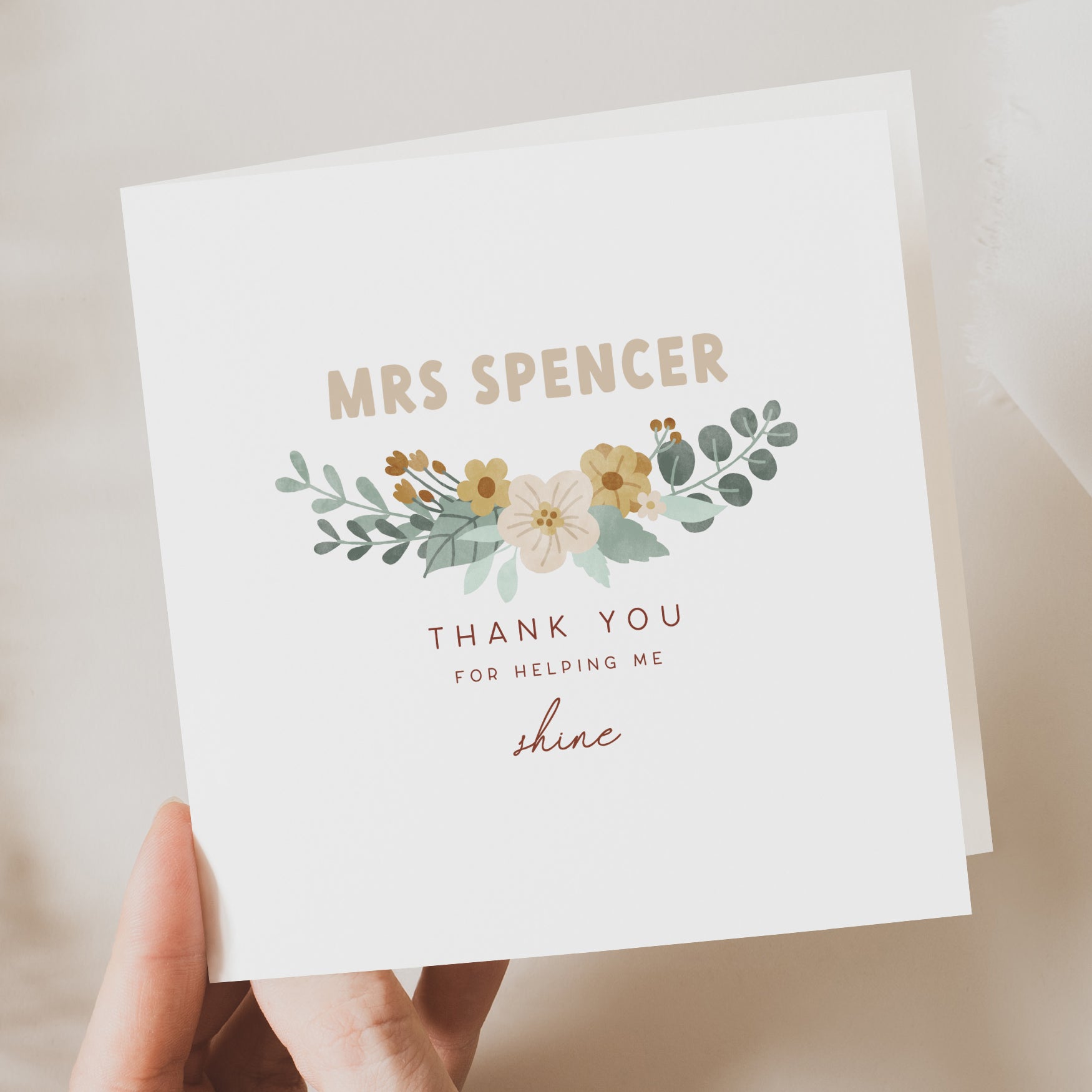 Greeting card with floral design and text held by a hand on a neutral background