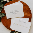 White envelopes with personalized text on a wooden surface with greenery