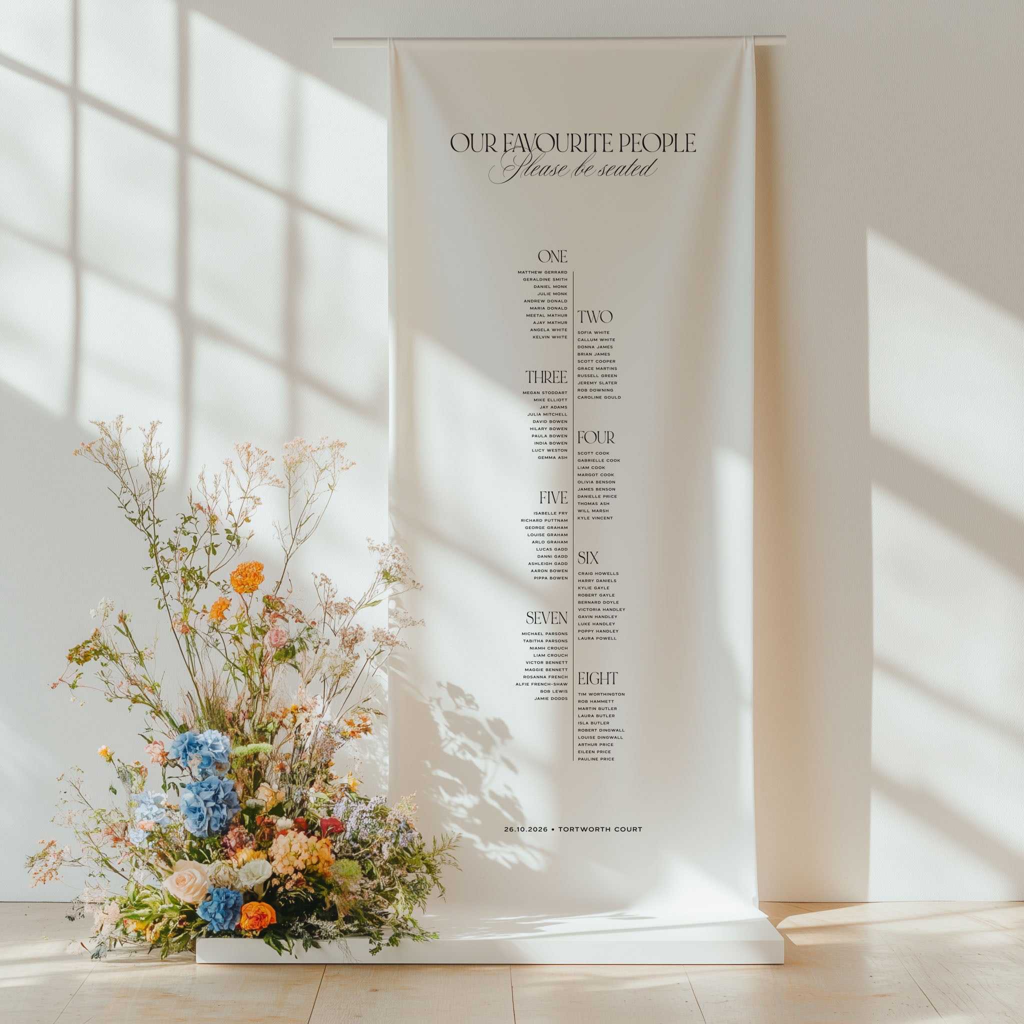 Cotton and linen wedding seating plan hanging on a stand with floral arrangement