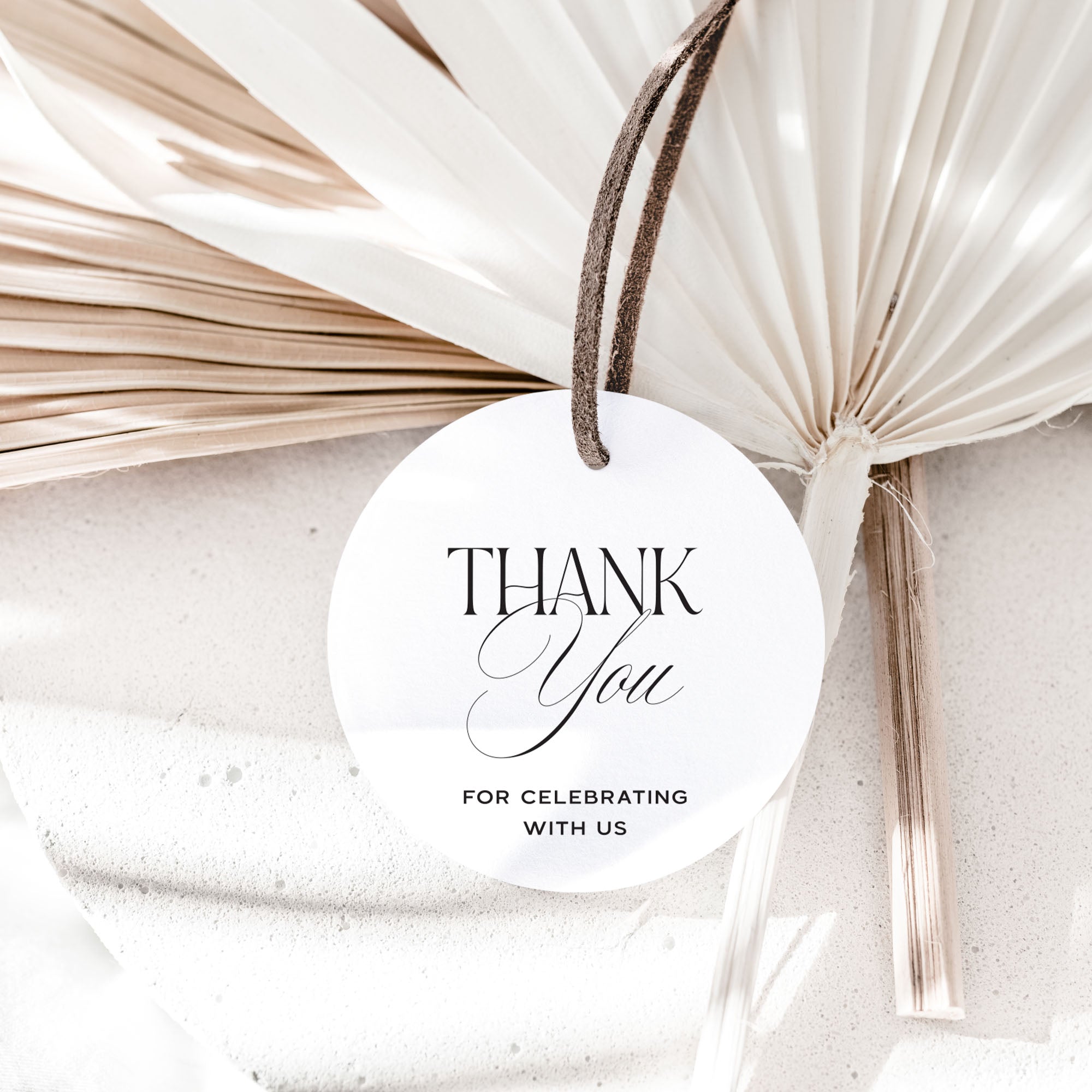 Round white card with 'Thank You for Celebrating with Us' text, tied with a string against a textured beige background.