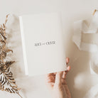 Hand holding a white card with 'ALICE and OLIVER' text on a light background