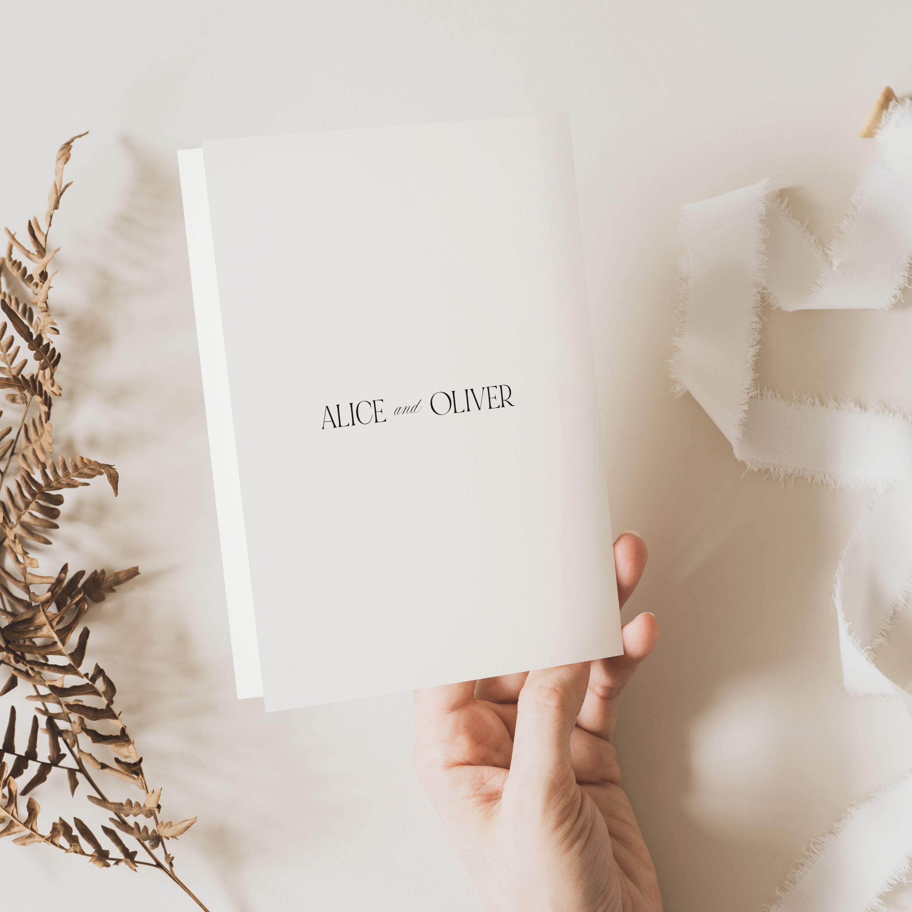 Hand holding a white card with 'ALICE and OLIVER' text on a light background