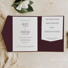 Wedding invitation suite with a maroon pocketfold on a textured surface.