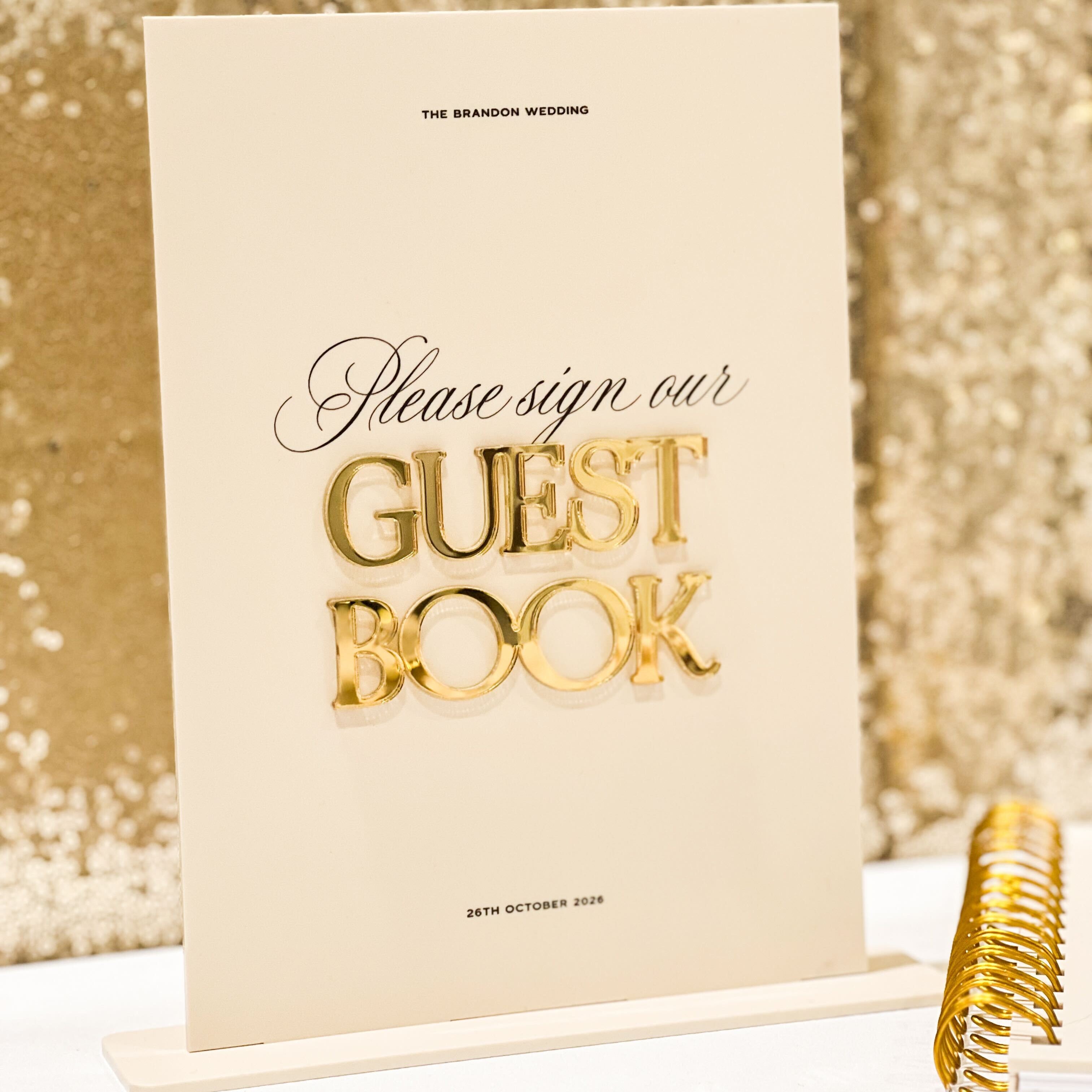 Beige guest book with gold text 'Please sign our Guest Book' on a glittery gold background