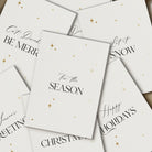 Stack of white Christmas cards with black text and gold stars on a white background