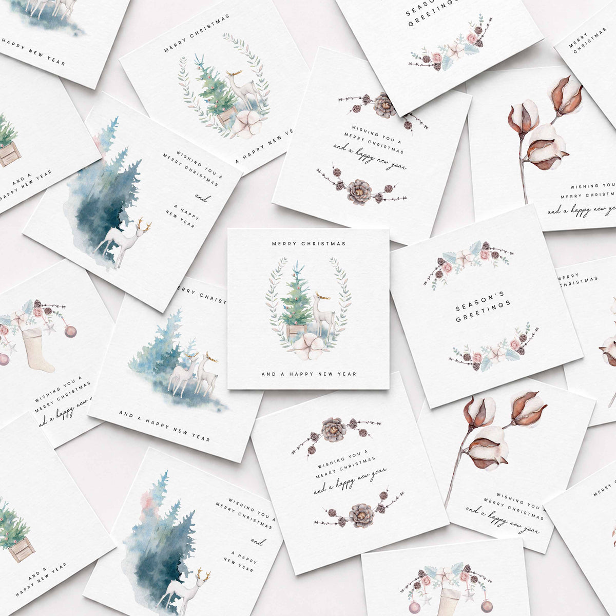 A flat-lay arrangement of multiple white Christmas greeting cards featuring delicate watercolor illustrations of Christmas trees, floral wreaths, pinecones, and holiday motifs on a light background.