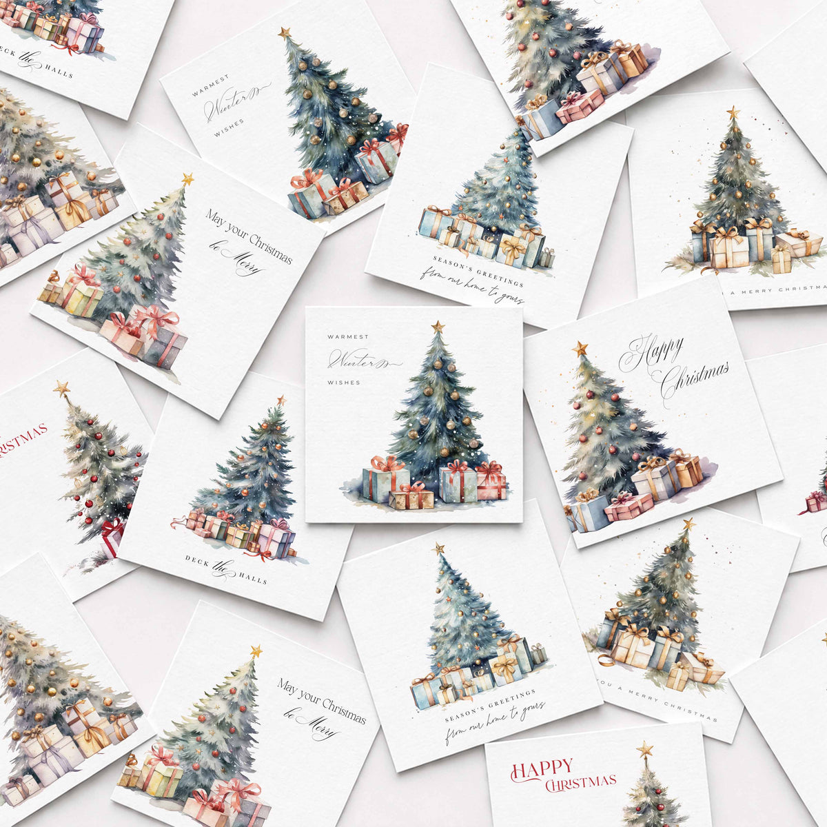 A flat-lay arrangement of multiple white Christmas greeting cards scattered on a light background. Each card features a watercolor illustration of a decorated Christmas tree with wrapped presents, with holiday greetings such as 'Happy Christmas' and 'Merry Christmas' in elegant script.
