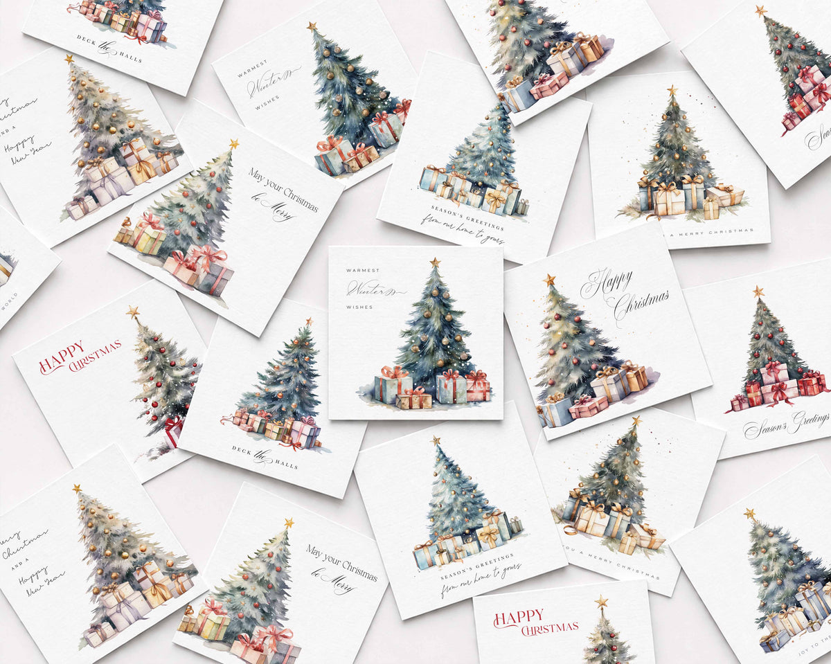 A flat-lay arrangement of multiple white Christmas greeting cards scattered on a light background. Each card features a watercolor illustration of a decorated Christmas tree with wrapped presents, with holiday greetings such as 'Happy Christmas' and 'Merry Christmas' in elegant script.