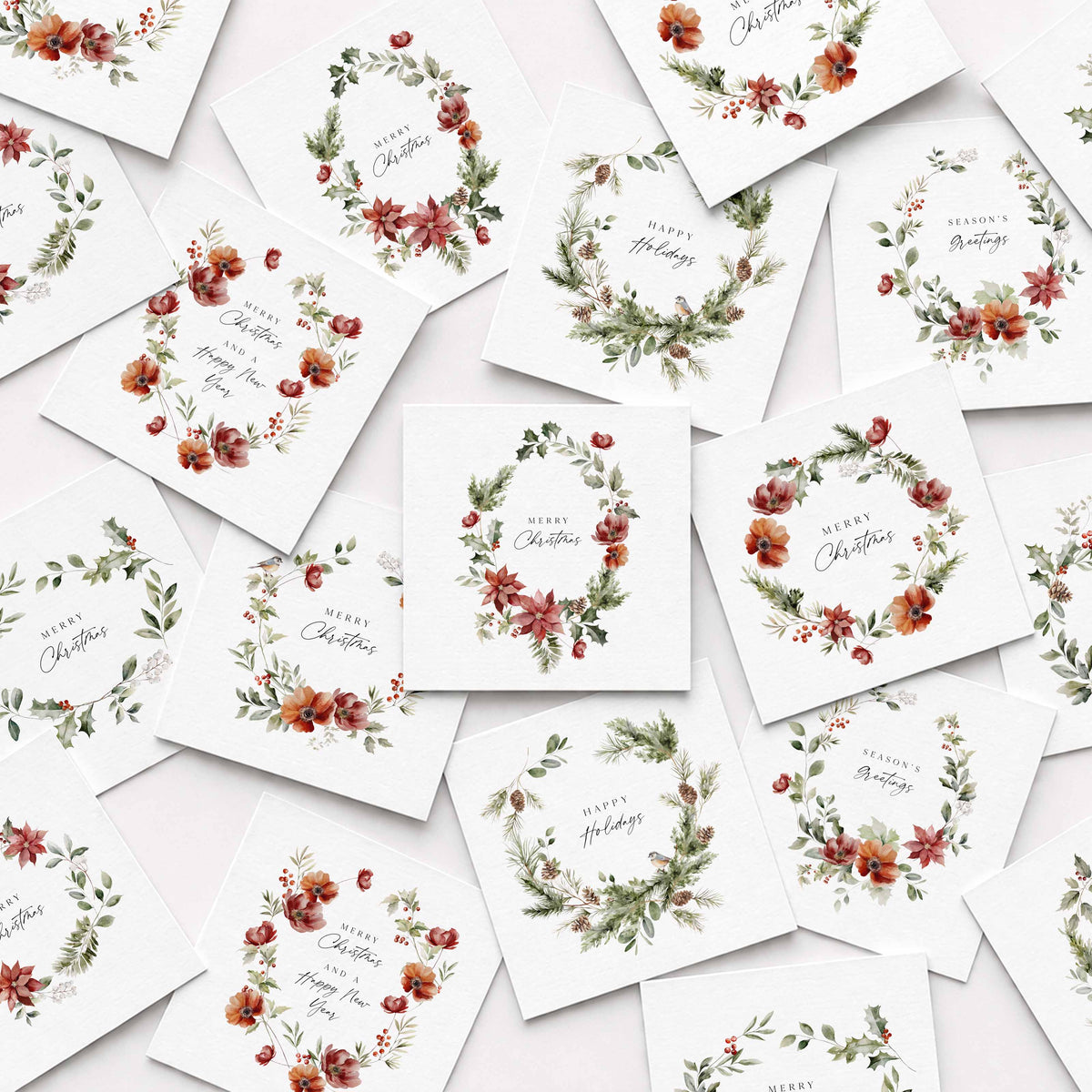 A flat-lay arrangement of multiple white square Christmas cards scattered on a light background, each printed with a watercolor floral wreath and holiday greeting text.