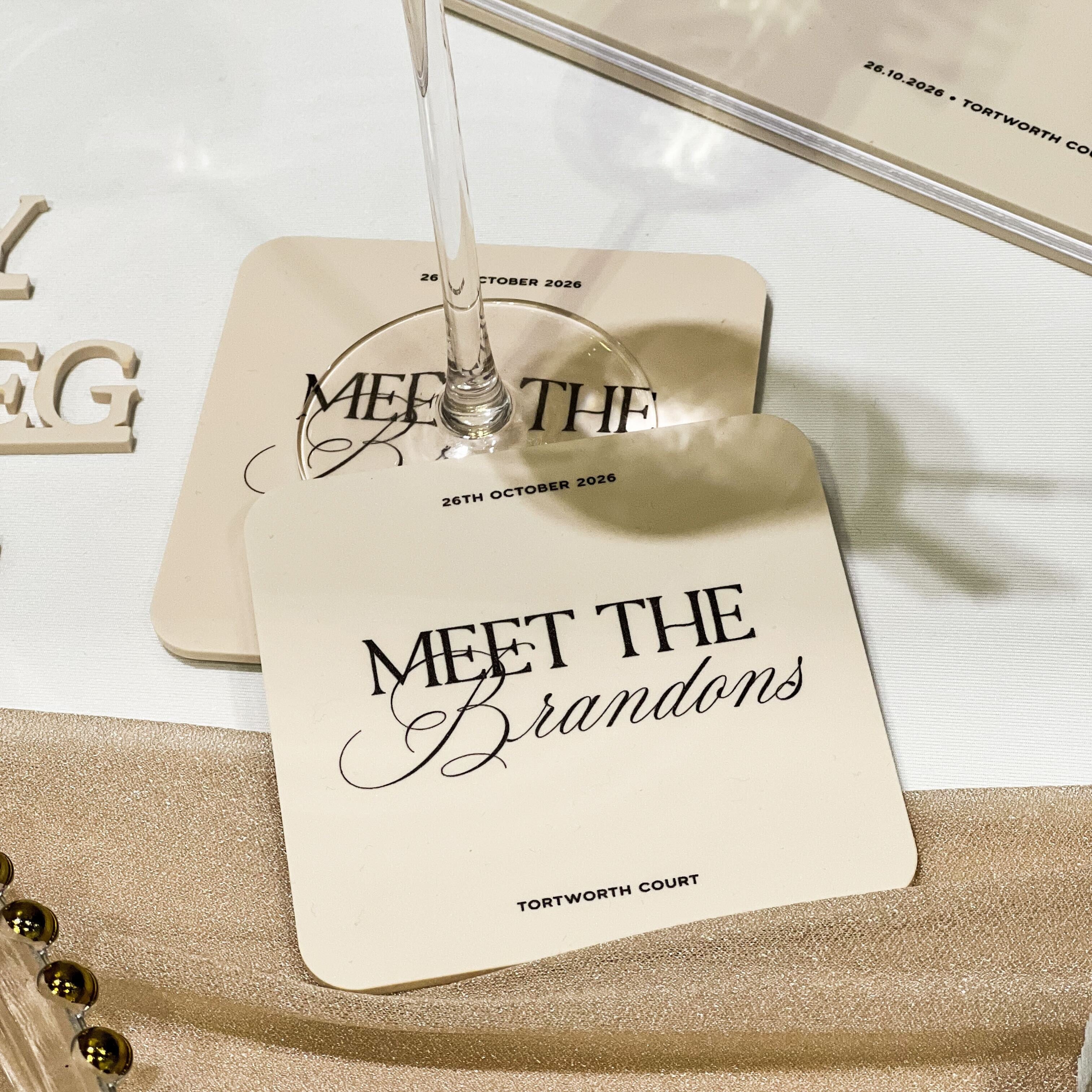 Coasters with 'Meet the Brandons' text on a glass of wine, placed on a textured surface.