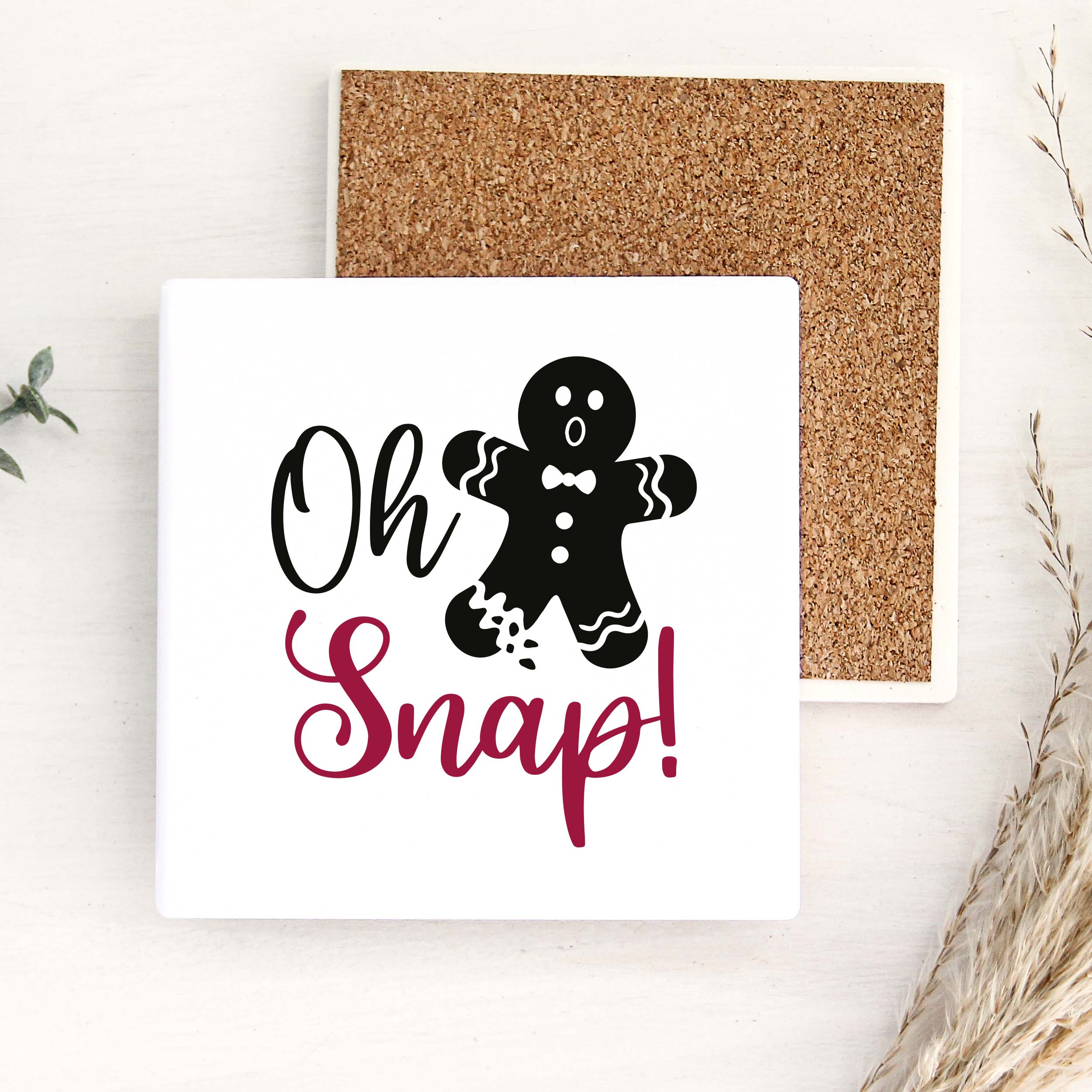 A square white snap card with a black gingerbread man illustration and the words 'Oh Snap!' in black and dark pink script, shown with a cork backing on a light wood surface.