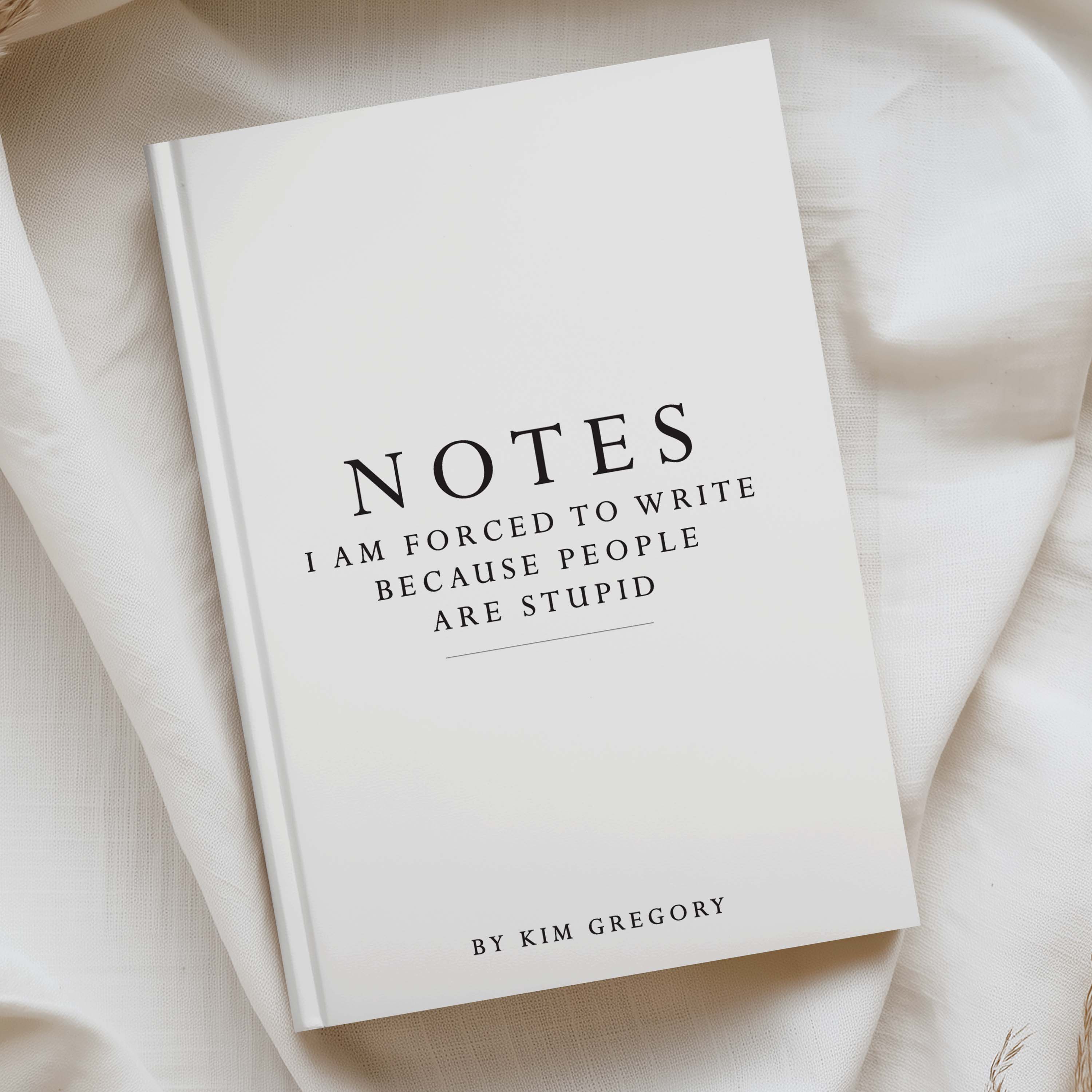 A hardcover notebook titled 'NOTES I AM FORCED TO WRITE BECAUSE PEOPLE ARE STUPID' by Kim Gregory, displayed on draped cream-colored fabric.