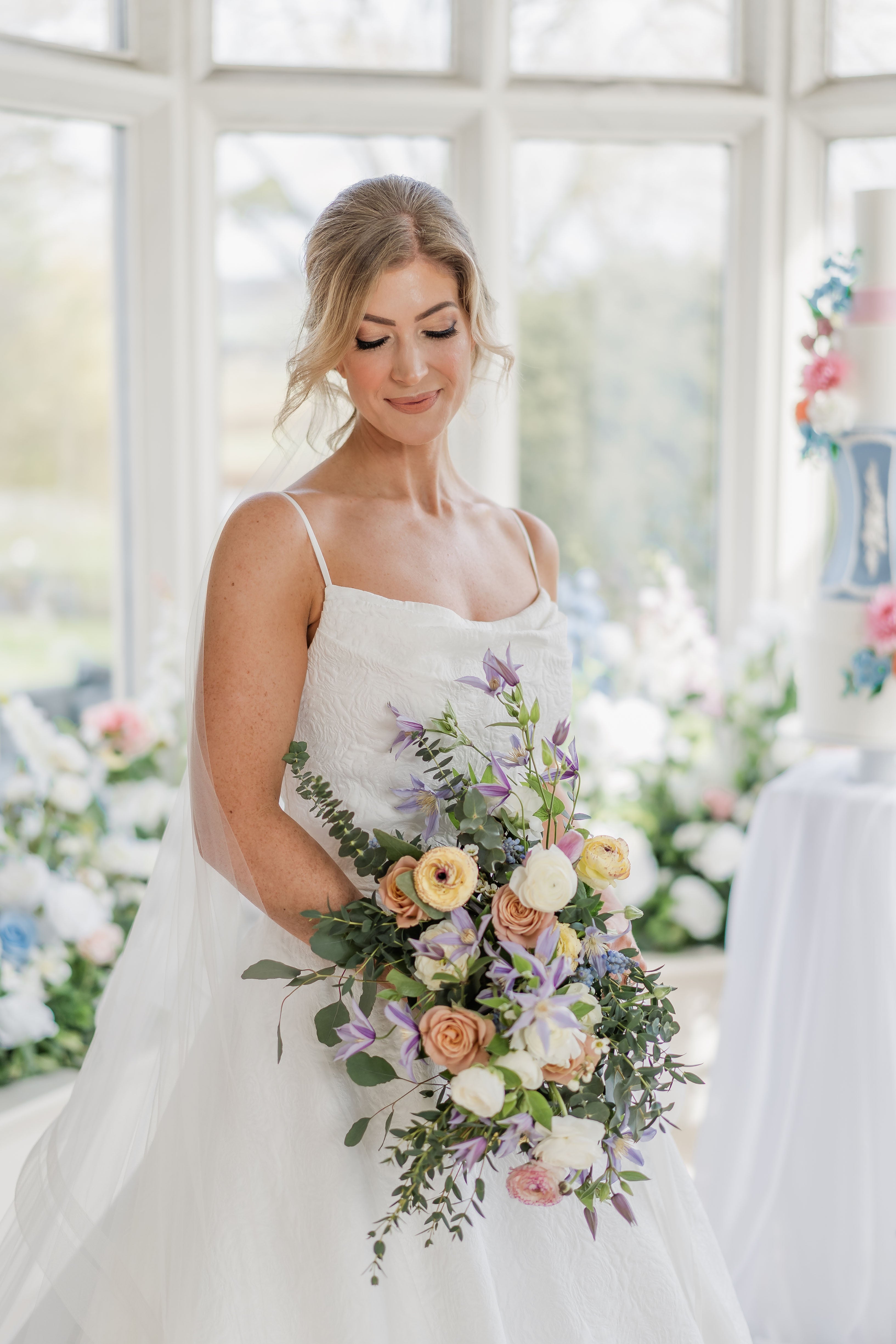 bride with large floral bouquet of pastel coloured flowers, in a large bay window for regency bridgerton style wedding