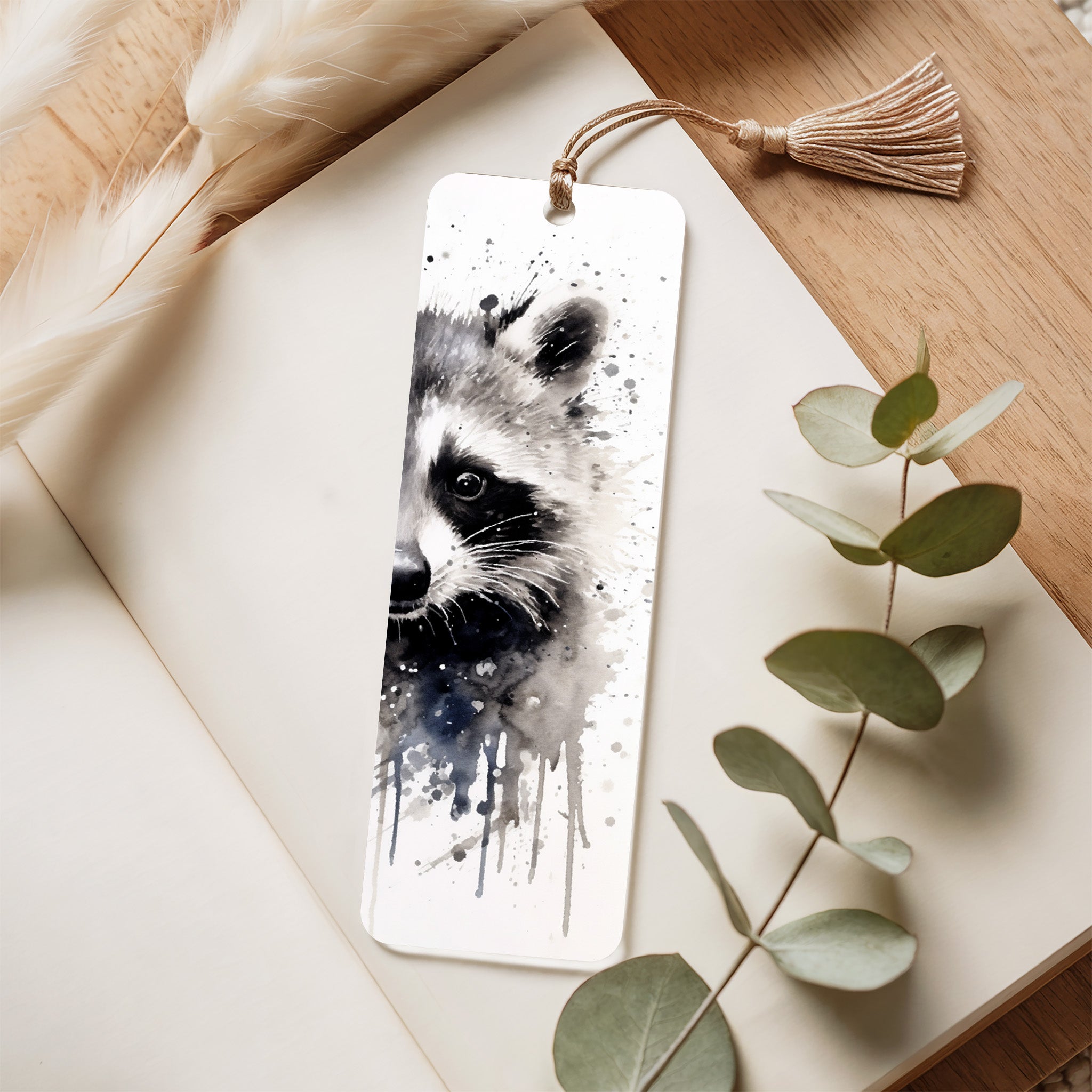 Bookmark with raccoon design on a wooden surface with eucalyptus leaves