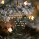 Clear acrylic Christmas ornament with text overlay on a blurred Christmas tree background