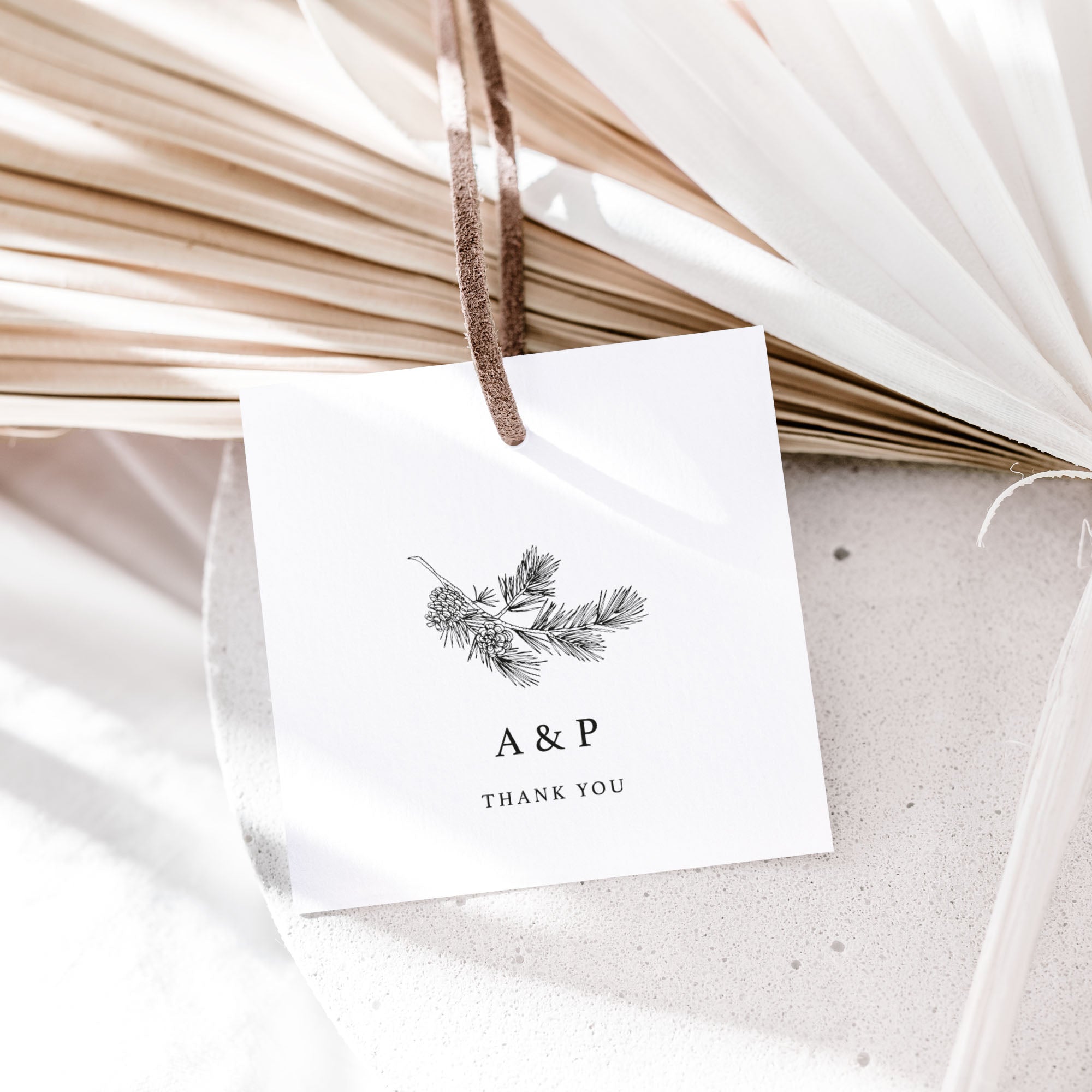 White favour tag with monogram and 'Thank You' text, hanging on dried plants.