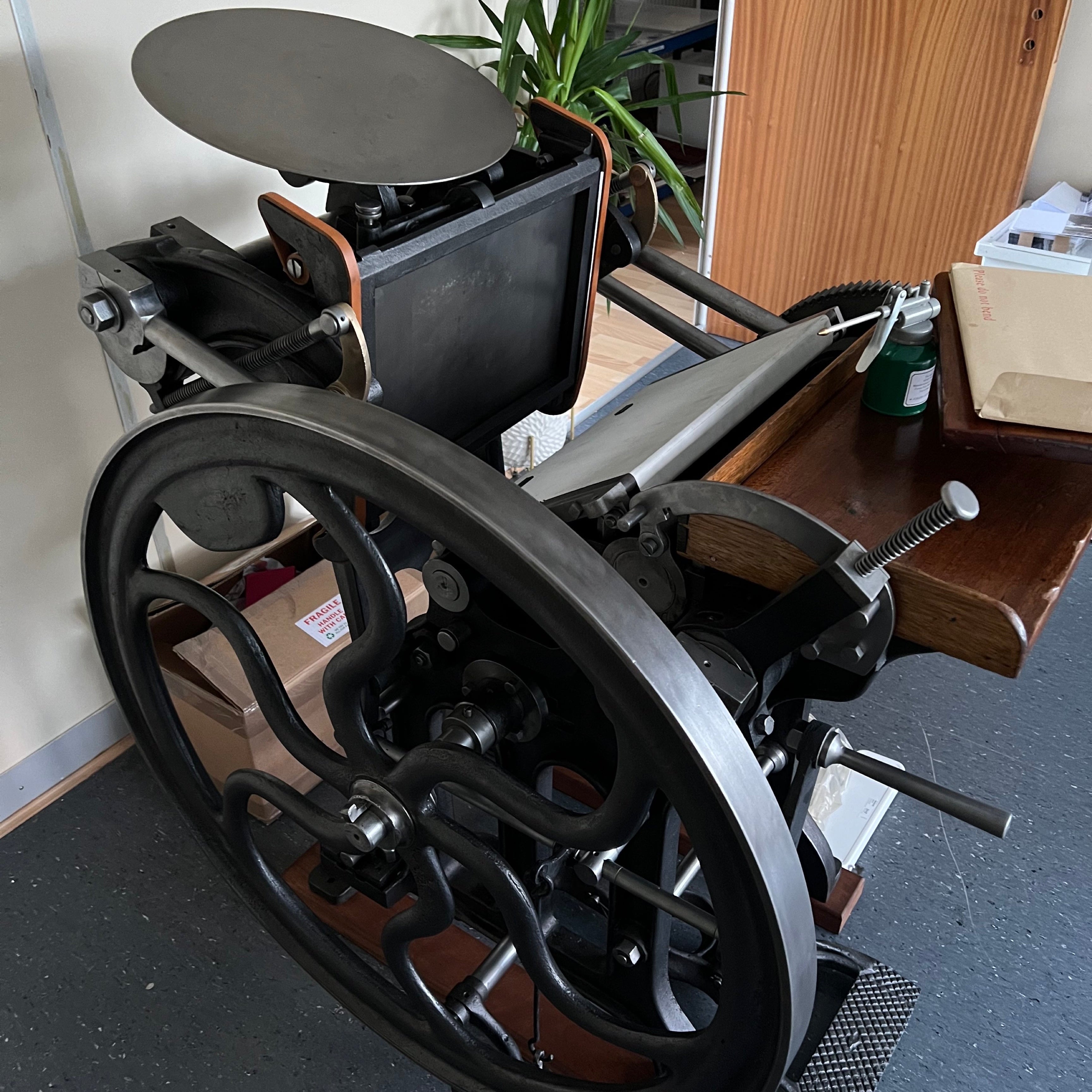 Vintage printing press in a room with boxes and a plant