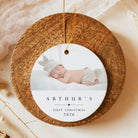A round wooden Christmas ornament with a hanging gold string, featuring a printed photo of a sleeping newborn baby and the text 'ARTHUR'S FIRST CHRISTMAS 2026' on a warm beige background.