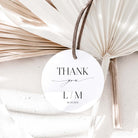 Round white card with 'Thank you L/M' text, tied with a string against a textured beige background.