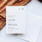 A minimalist wedding save-the-date card with elegant black typography on a white card, styled on a light marble surface next to an envelope and a textured brown fabric.