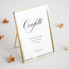 Gold-framed sign with 'Confetti' and wedding details on a light background