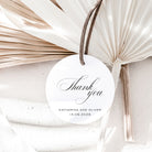 Round white card with 'Thank you' text, tied with a string, on a textured surface with dried leaves.