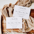 Two white save the date cards in landscape orientation, shown on neutral coloured fabric, wooden display board, gold wax stamp, wax seals and pampass grass