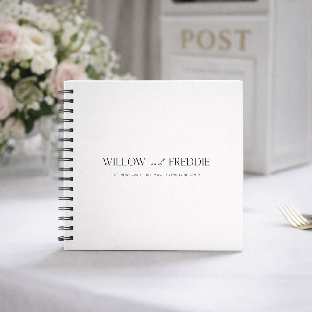 White spiral-bound guest book for wedding with text on a white surface with flowers and a box in the background
