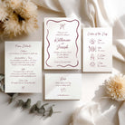 A flat lay of a whimsical wedding invitation suite showing an invitation, details card, itinerary and RSVP card
