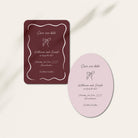 A wedding save-the-date card set displayed on a light beige background with soft shadows. The set includes a dark burgundy rectangular card with a white decorative border and a light pink oval card with a matching white border.