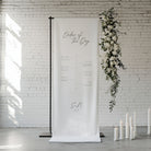 White banner with 'Order of the Day' text against a white brick wall with floral decorations.