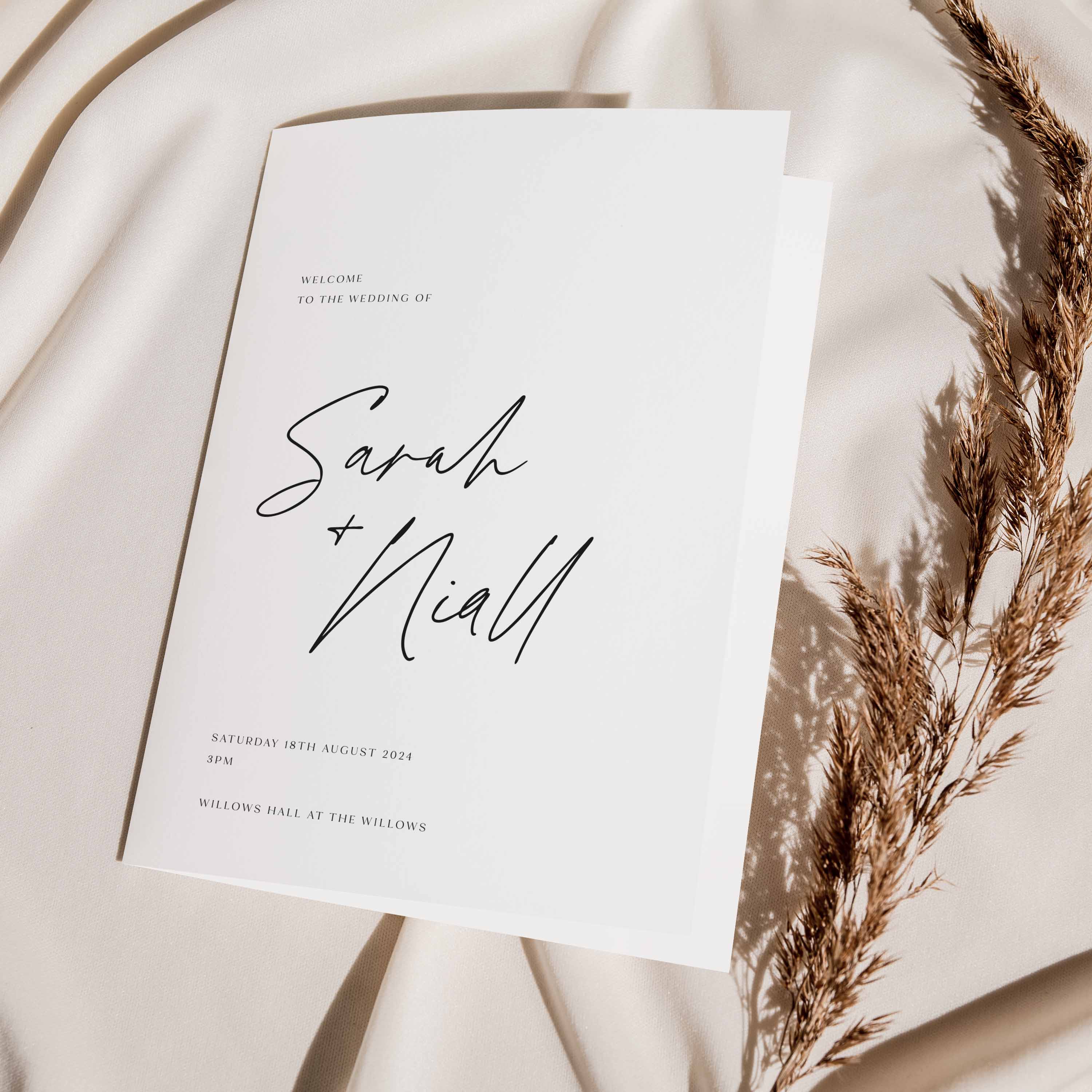 Wedding order of service booklet with 'Sarah + Niall' on a soft beige background with dried grasses.
