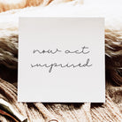 White card with 'now act surprised' text on a textured brown surface