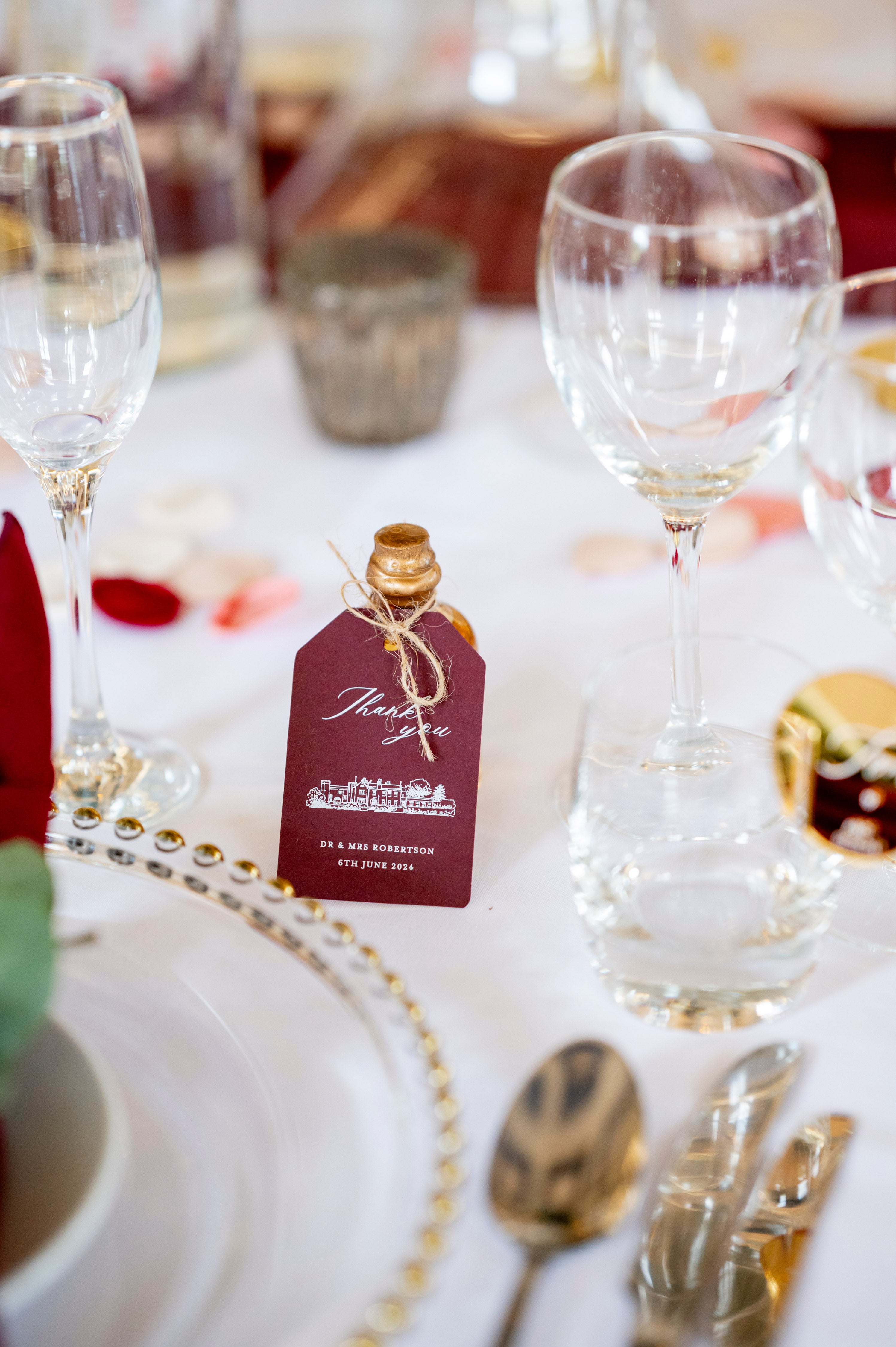 Decorative table setting with wine glasses, place card, and cutlery on a white tablecloth.