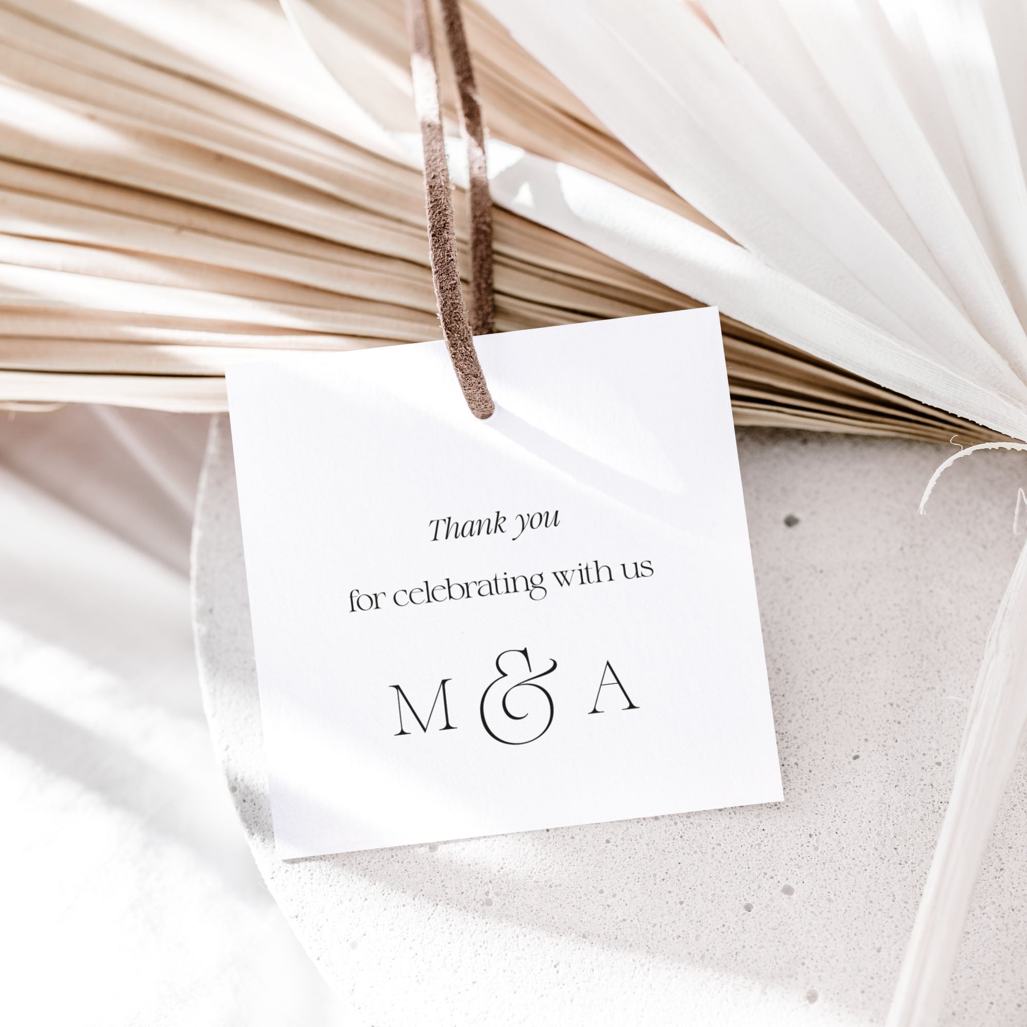 White card with 'Thank you for celebrating with us M & A' text, hanging on dried palm leaves.