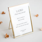 Gold-framed wedding sign for ladies toileteries with text on a light gray background
