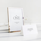 Gold-framed table number card with 'ONE' and a name card below on a white surface.