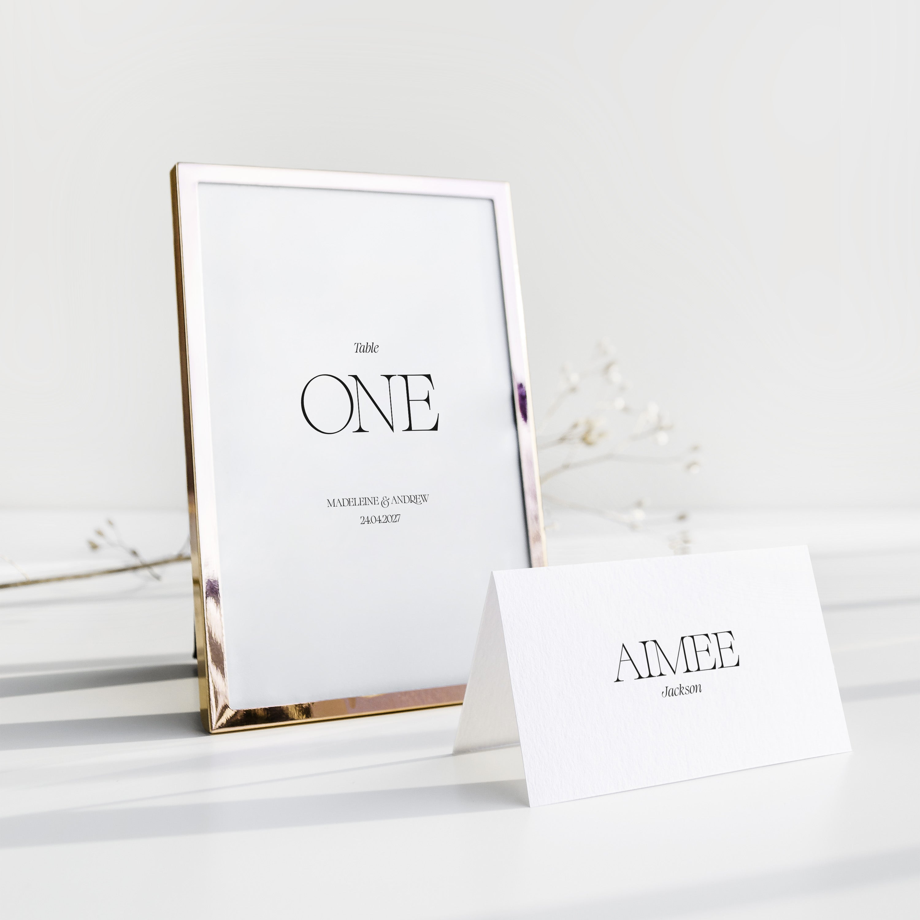 Gold-framed table number card with 'ONE' and a name card below on a white surface.